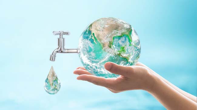 A person's hand holding a globe of the earth with a water faucet sticking out of it